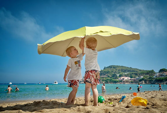 Dos niños bajo una sombrilla en la playa - juegos de agua y arena